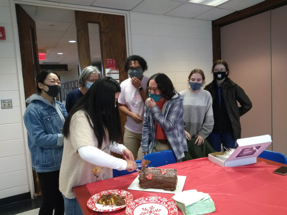 students and their professor gathered around a traditional yule log cake