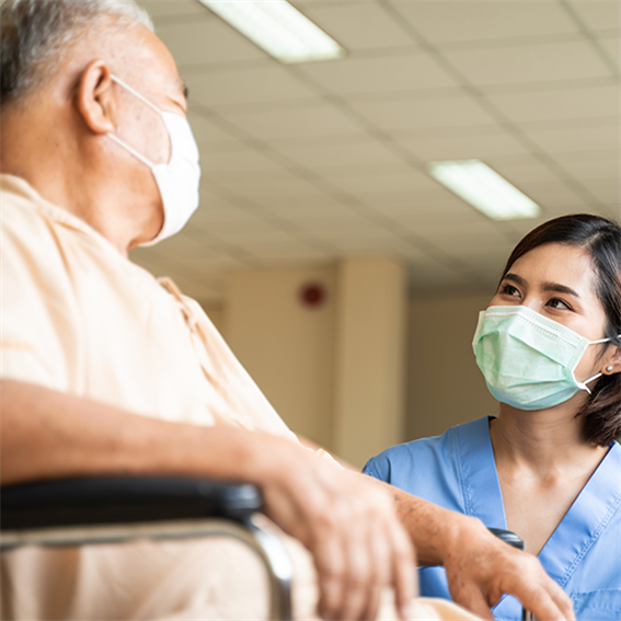 a woman in scrubs talks to a man in a wheelchair