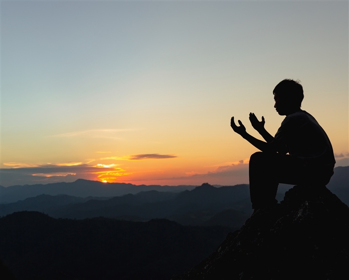 young male sitting on rock at sunset