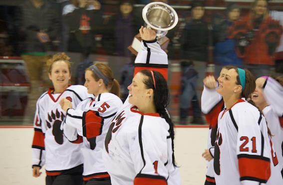 the women's hockey team celebrating on the ice with a trophy