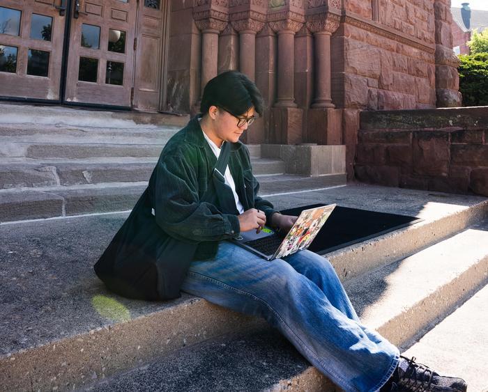 a student sitting on steps outside on a laptop