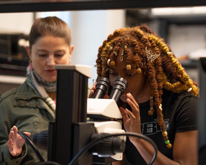 student peering through microscope