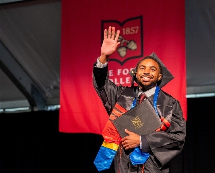 Grad in regalia holding diploma and waving