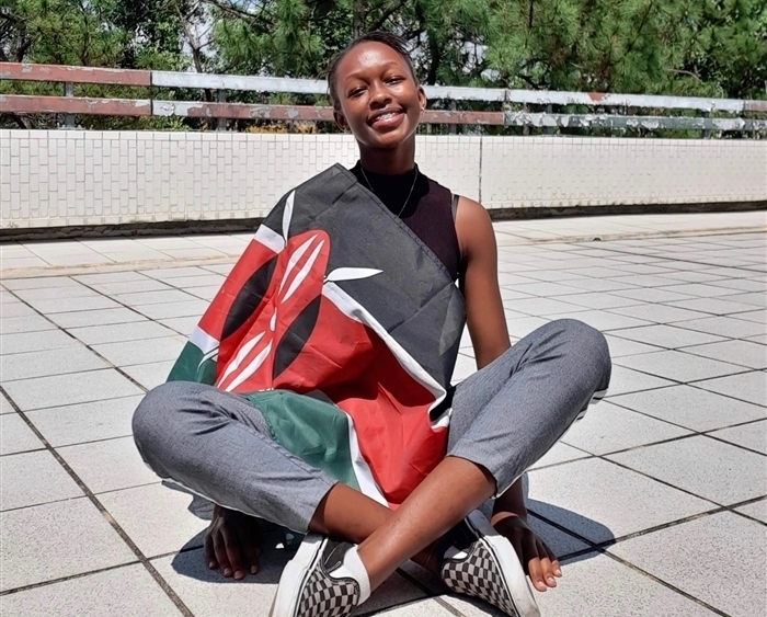 Hawi Odhiambo seated cross-legged on ground wrapped in Kenyan flag