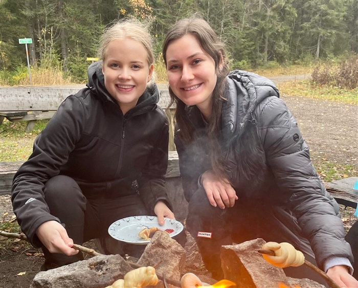 Two young women outside in Finland roasting sausages over a fire