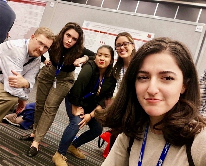 professor and four students mugging for selfie in front of their research poster