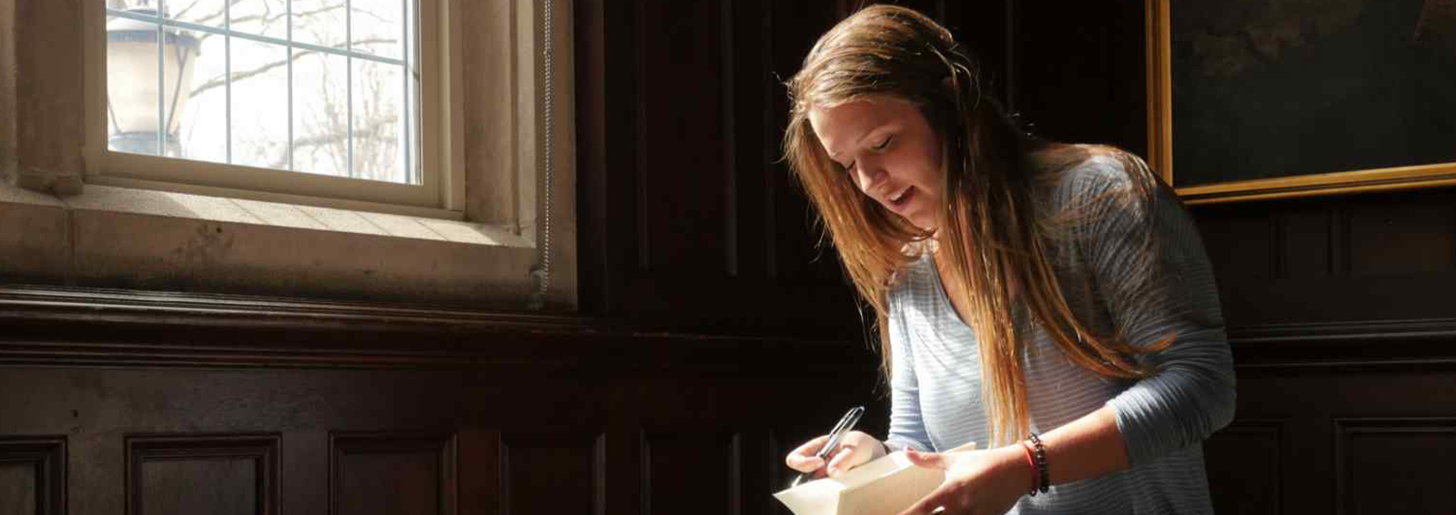 a woman reading a book in front of a window in sunlight