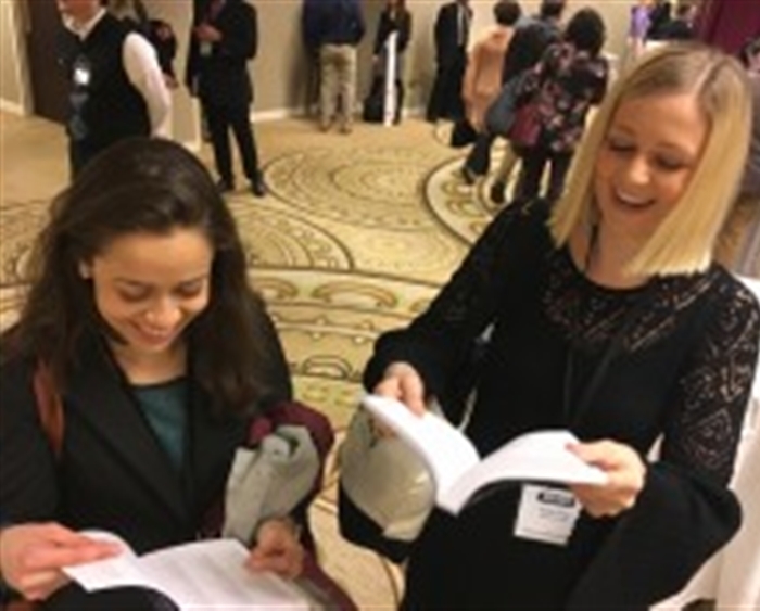 two students looking at their names in program at conference